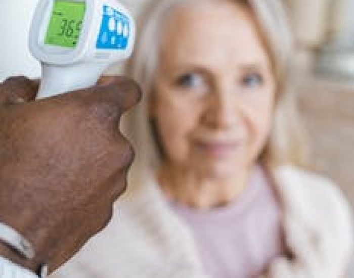 Nurse checks temperature of senior woman using an infrared thermometer.